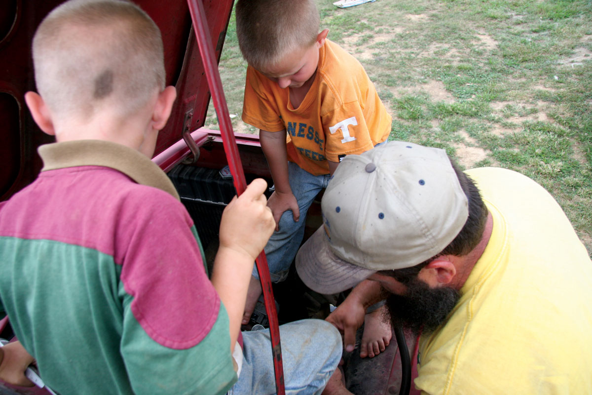 A dad working on his vehicle with two of his little boys looking on