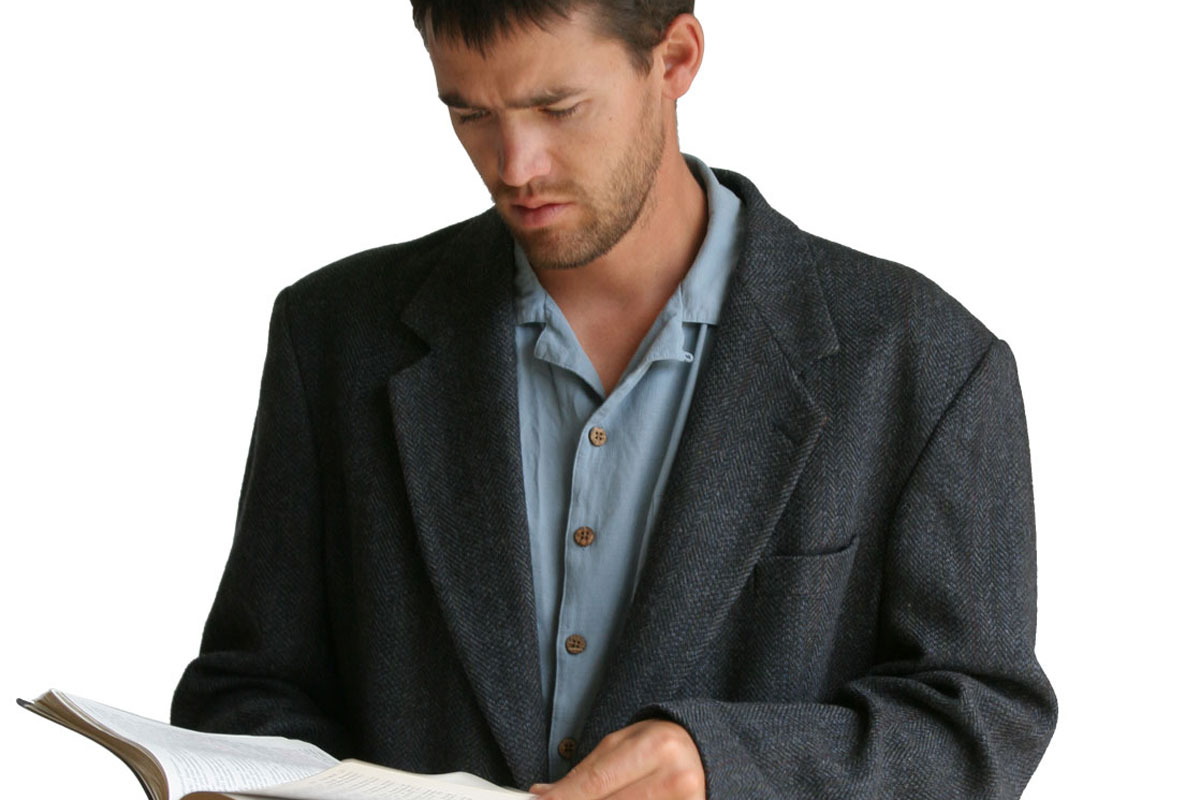Man standing in collard shirt and suit coat, reading the King James Version Bible