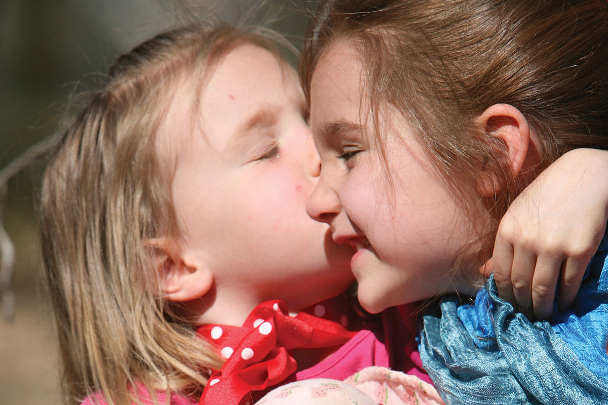 A little blonde haired girl giving her big sister a kiss