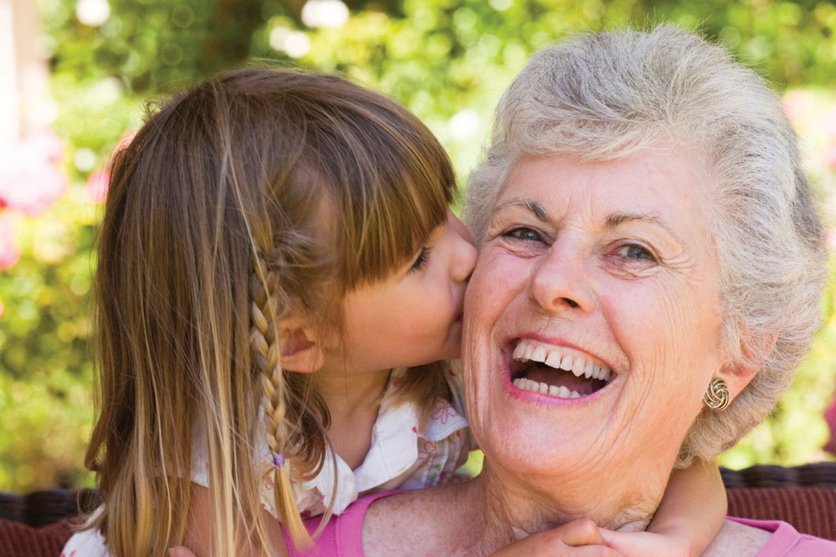 A laughing grandmother being kissed by her blonde haired little granddaughter in pink