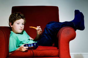 Boy on couch holding video game controller and slice of pizza