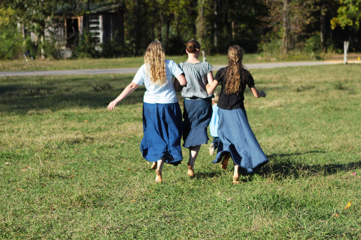 Three young girls skipping through a field.