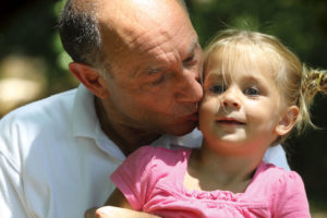 Grandfather planting a kiss on the cheek of his little blonde haired granddaughter